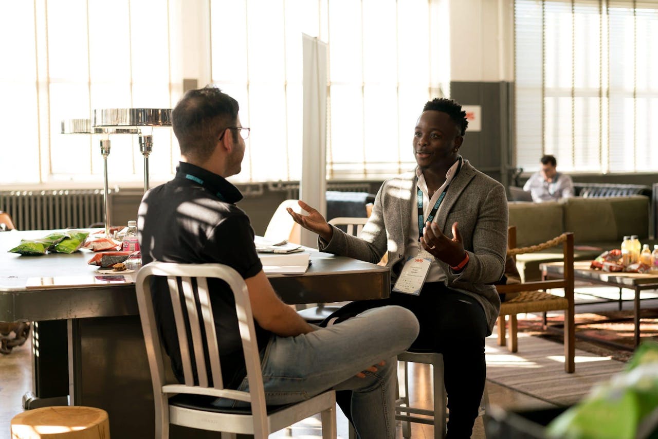 ours-journey Two men having a casual discussion in a bright indoor setting, highlighting mentorship.